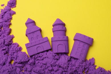 Castles made of kinetic sand on yellow background, flat lay