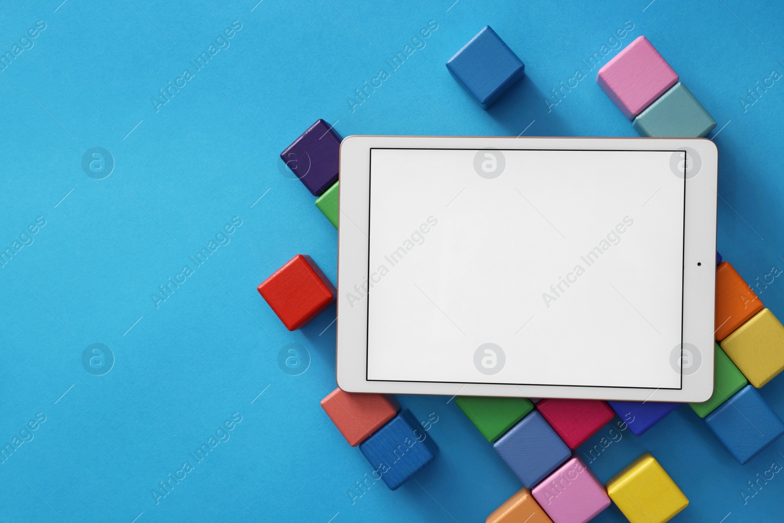 Photo of Modern tablet and cubes on light blue background, flat lay. Space for text