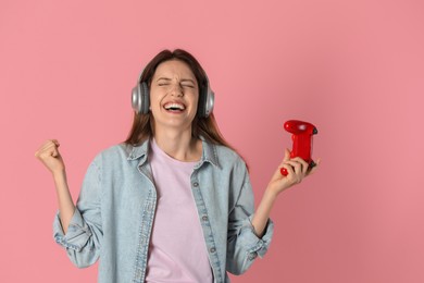 Photo of Emotional woman in headphones with game controller on pink background. Space for text