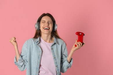 Emotional woman in headphones with game controller on pink background. Space for text