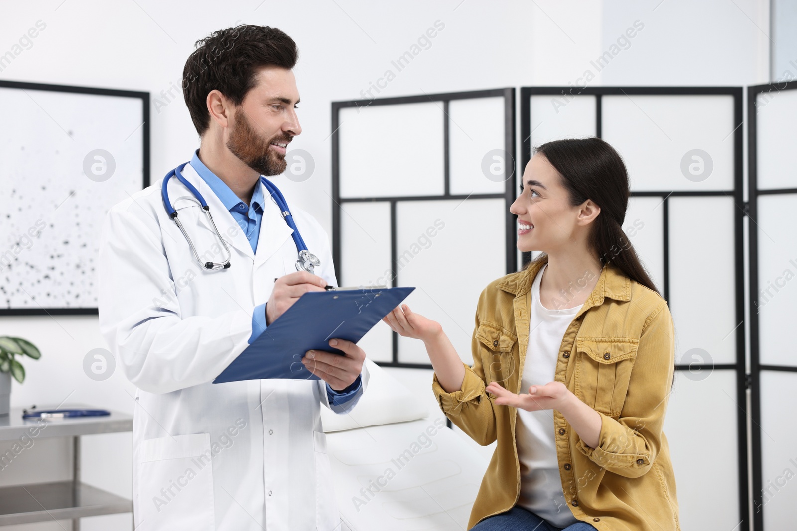 Photo of Doctor with clipboard consulting patient during appointment in clinic