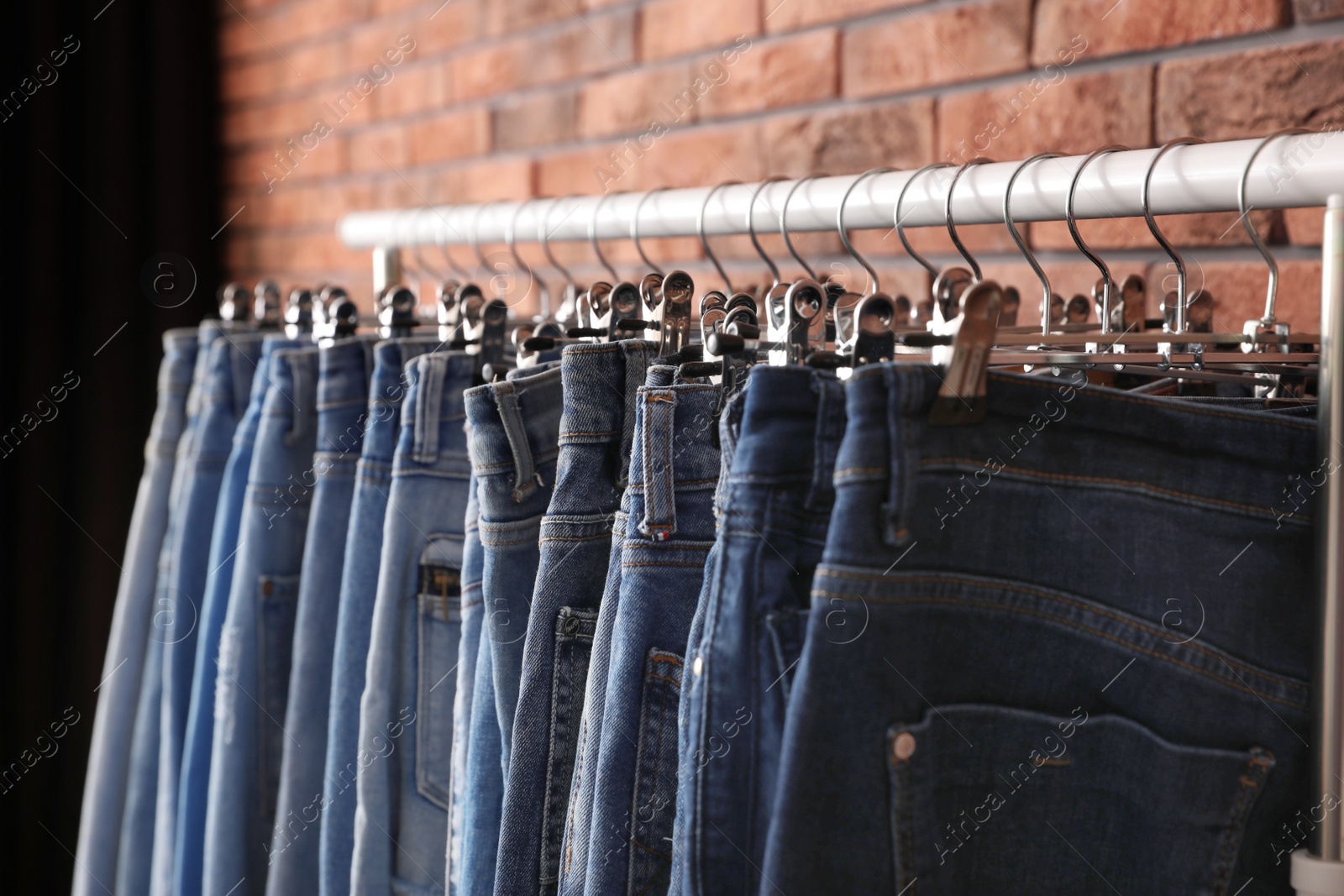 Photo of Rack with stylish jeans near brick wall, closeup