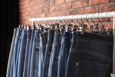 Photo of Rack with stylish jeans near brick wall, closeup