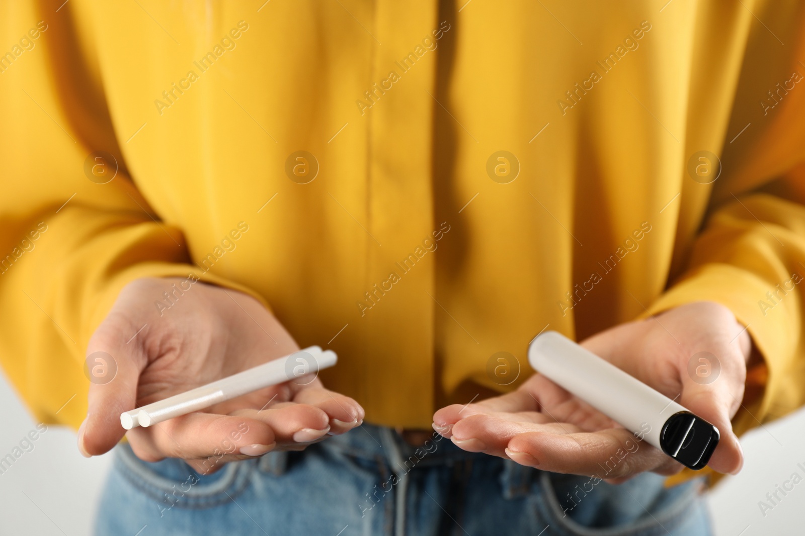 Photo of Woman with cigarettes and vaping device on light background, closeup. Smoking alternative