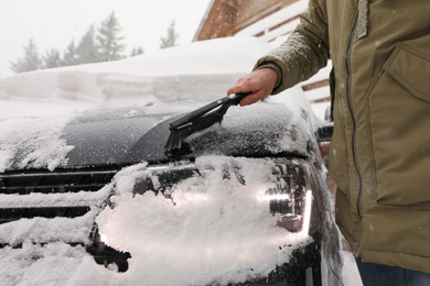 Photo of Young man cleaning snow from car outdoors on winter day, closeup