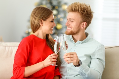 Photo of Happy young couple with glasses of champagne on sofa at home. Christmas celebration