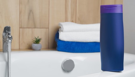 Photo of Purple bottle of bubble bath and towels on tub indoors, space for text