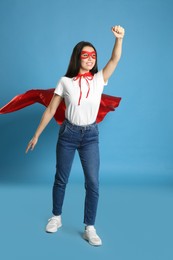 Photo of Confident young woman wearing superhero cape and mask on light blue background