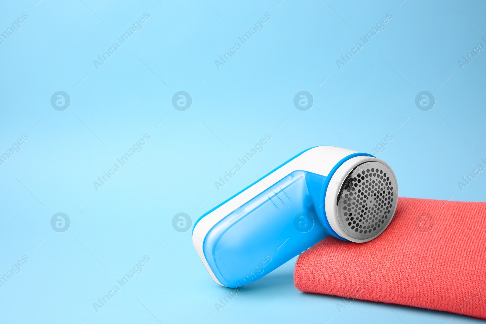 Photo of Modern fabric shaver and cloth with lint on light blue background. Space for text