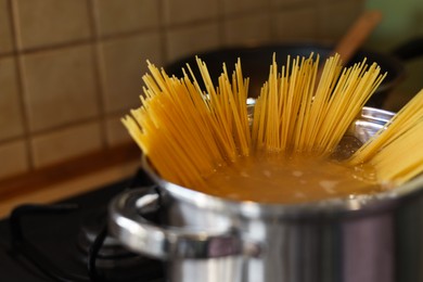 Photo of Shiny pot with water and spaghetti on stove indoors, closeup