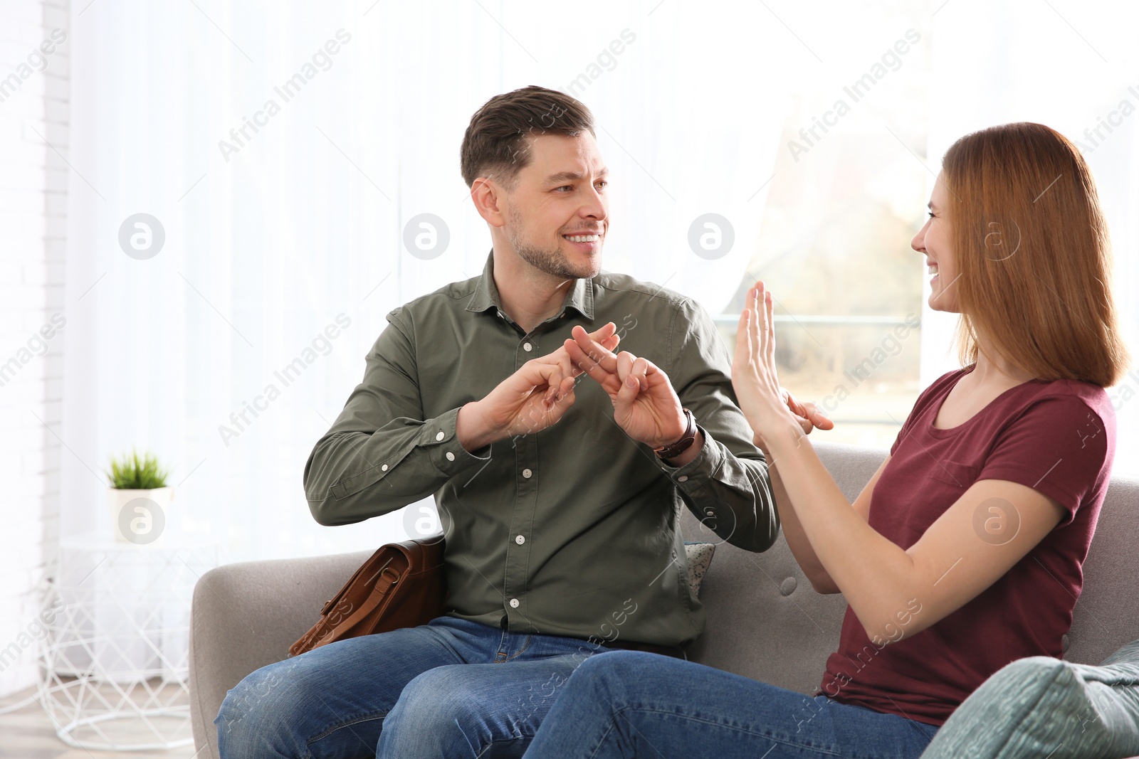 Photo of Hearing impaired friends using sign language for communication on sofa in living room