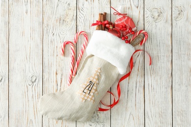 Photo of Christmas stocking with festive decor and treats on white wooden table, flat lay. Advent calendar