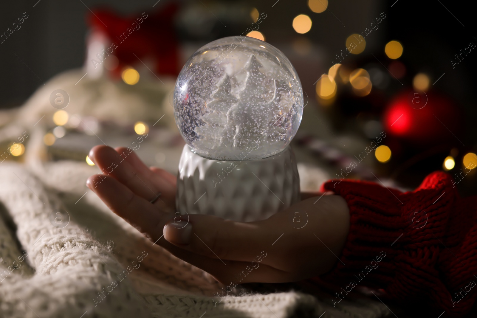 Photo of Woman holding Christmas snow globe on blurred background, closeup