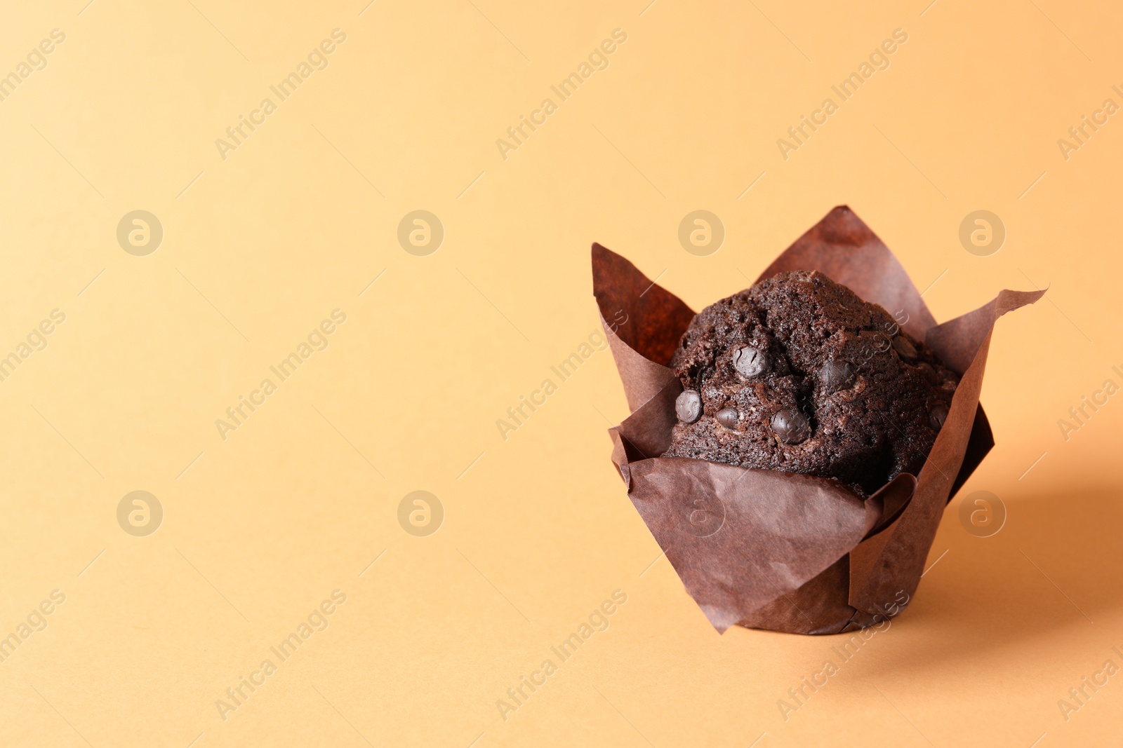 Photo of Tasty chocolate muffin on pale orange background, space for text