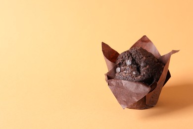 Photo of Tasty chocolate muffin on pale orange background, space for text