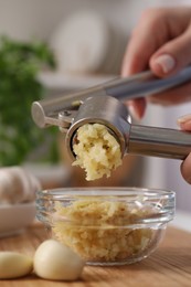 Woman squeezing garlic with press at wooden table indoors, closeup