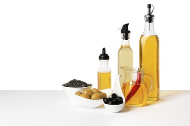 Photo of Bottles of different cooking oils, olives and sunflower seeds on white background, space for text
