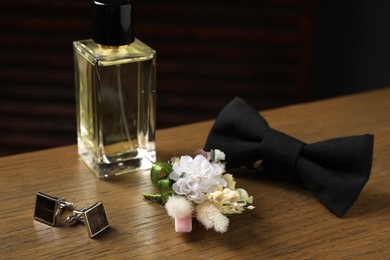 Wedding stuff. Stylish boutonniere, perfume bottle, bow tie and cufflinks on wooden table, closeup