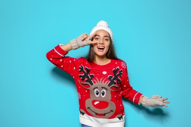 Young woman in Christmas sweater and knitted hat on color background