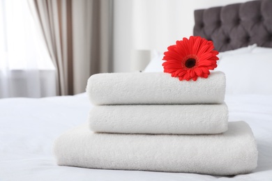 Stack of fresh towels with flower on bed indoors. Space for text