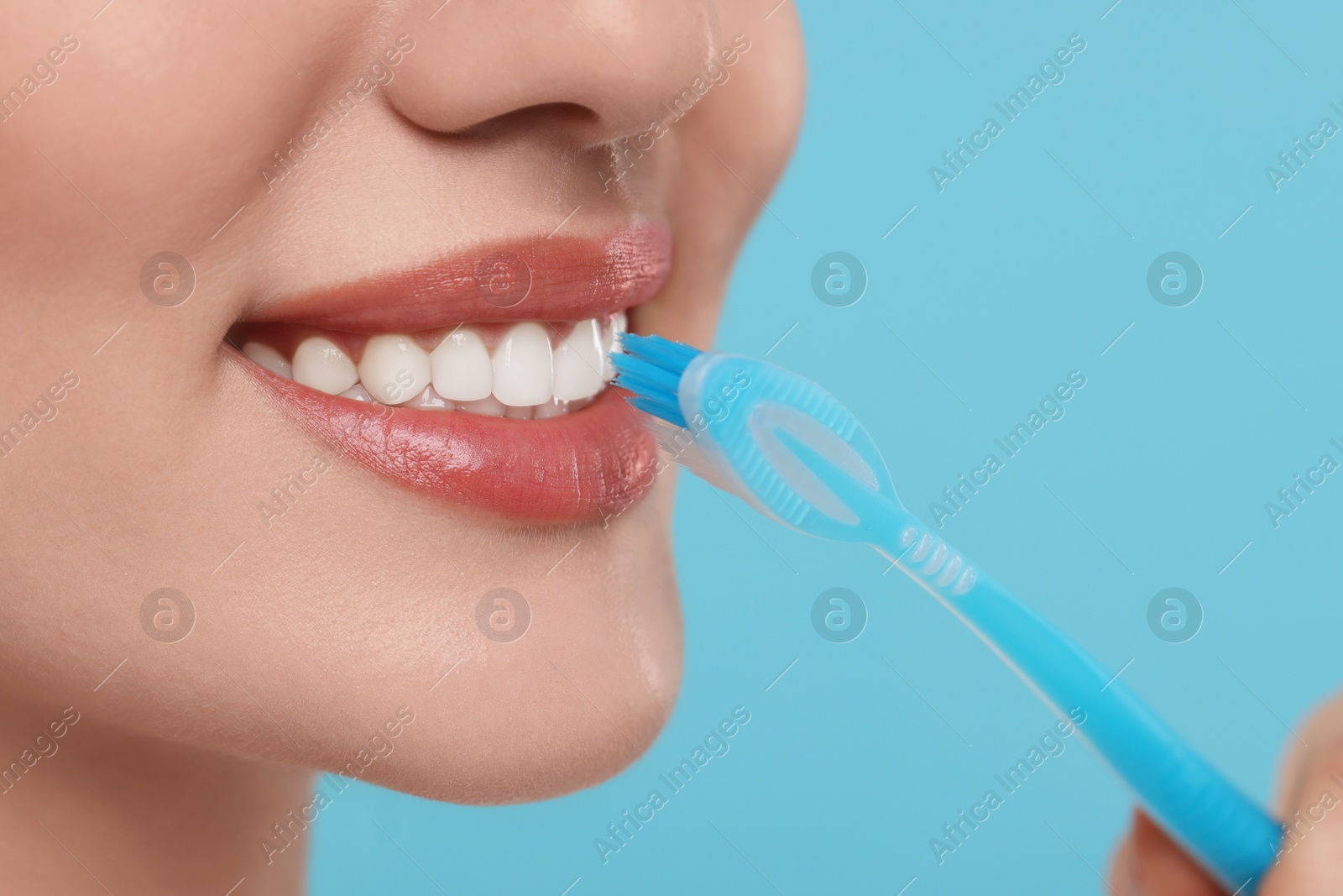 Photo of Woman brushing her teeth with plastic toothbrush on light blue background, closeup