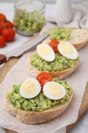 Photo of Delicious sandwiches with guacamole, eggs and tomatoes on parchment paper, closeup