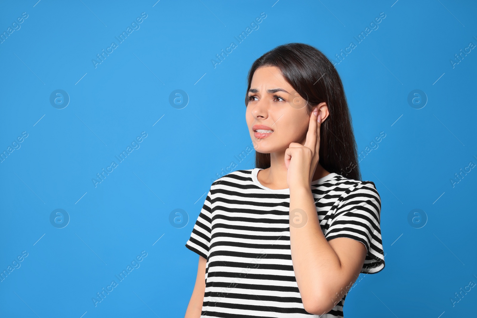 Photo of Young woman suffering from ear pain on light blue background. Space for text