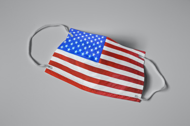 Image of Medical protective mask with USA flag pattern on light grey background, top view. Dangerous virus