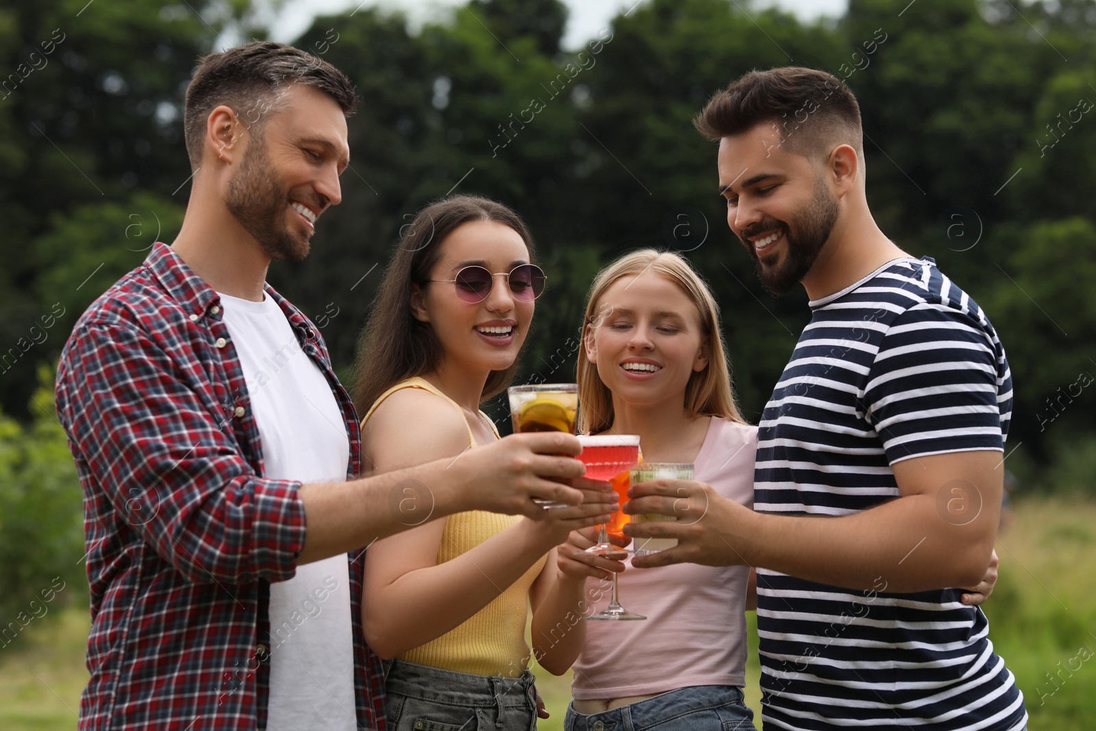 Photo of Happy friends clinking glasses with cocktails outdoors