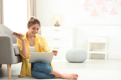 Photo of Young woman with smartphone using laptop at home