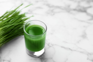 Photo of Glass of juice and fresh wheat grass on marble background. Space for text
