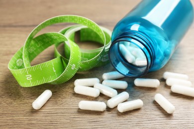 Photo of Jar of weight loss pills and measuring tape on wooden table, closeup