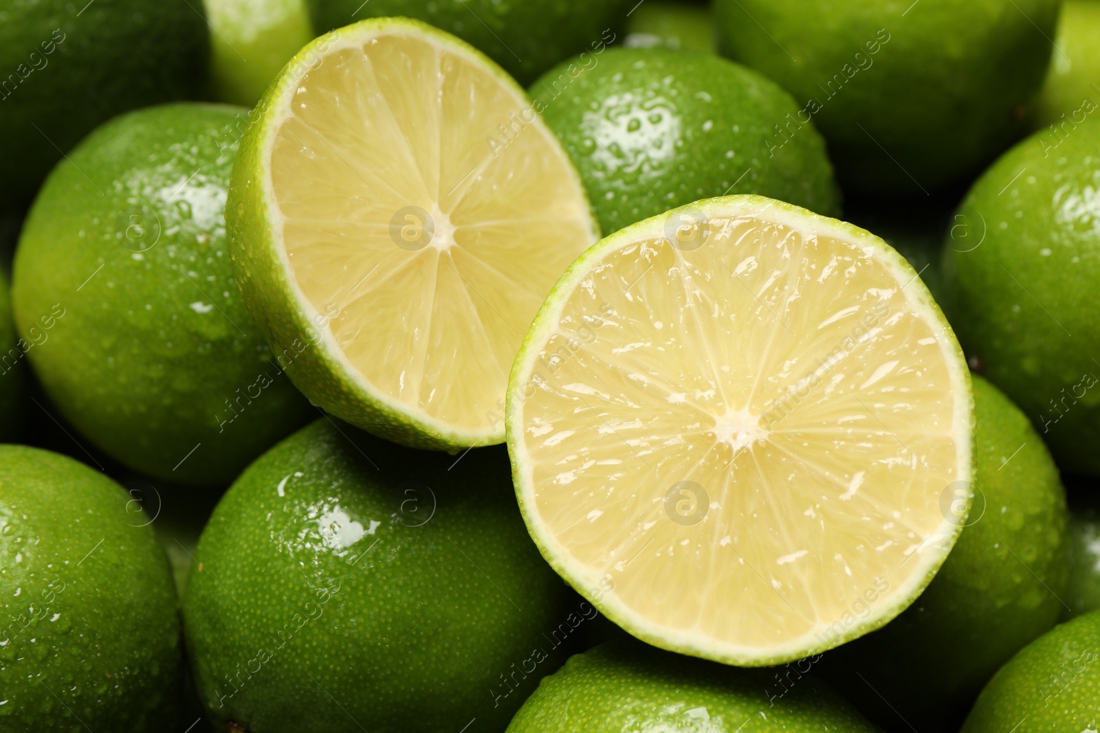 Photo of Whole and cut fresh limes with water drops as background, closeup