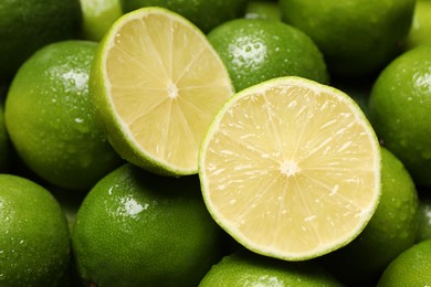 Whole and cut fresh limes with water drops as background, closeup