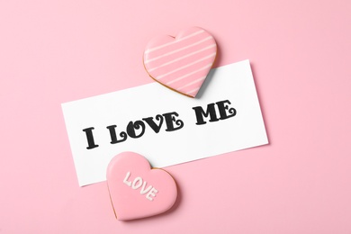 Paper with handwritten phrase I Love Me and heart shaped cookies on pink background, flat lay