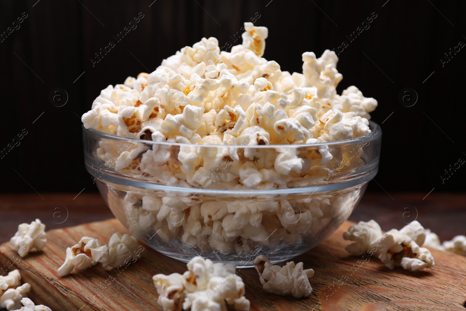 Photo of Bowl of tasty popcorn on wooden board, closeup