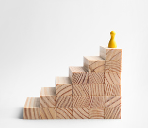 Photo of Yellow game piece on top of stairs against white background. Career promotion concept