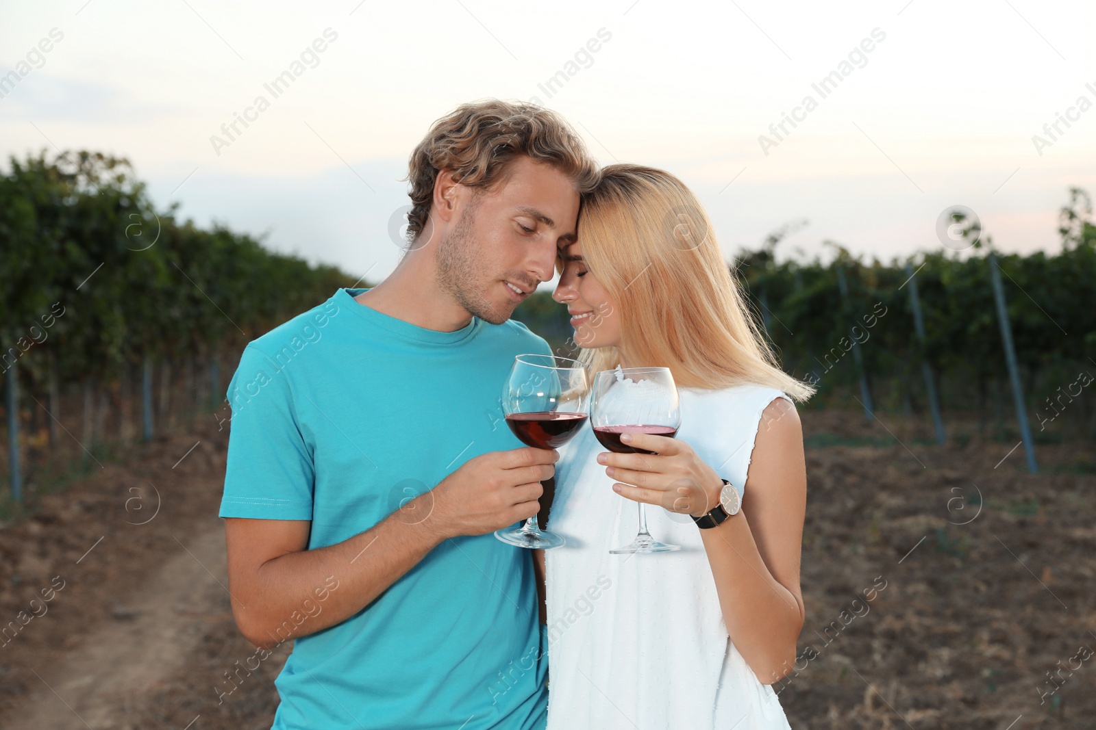 Photo of Young romantic couple holding glasses of wine at vineyard