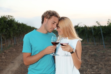 Young romantic couple holding glasses of wine at vineyard