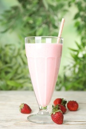 Tasty fresh milk shake with strawberries on white wooden table against blurred background