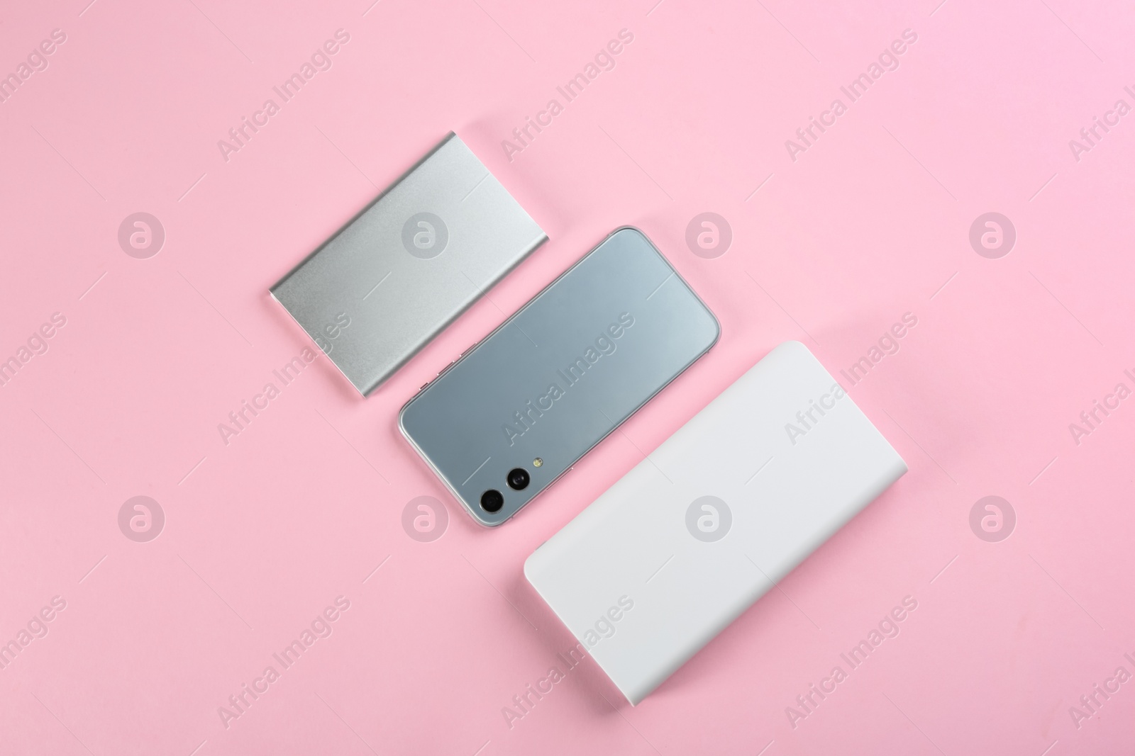 Photo of Mobile phone and portable chargers on pink background, flat lay