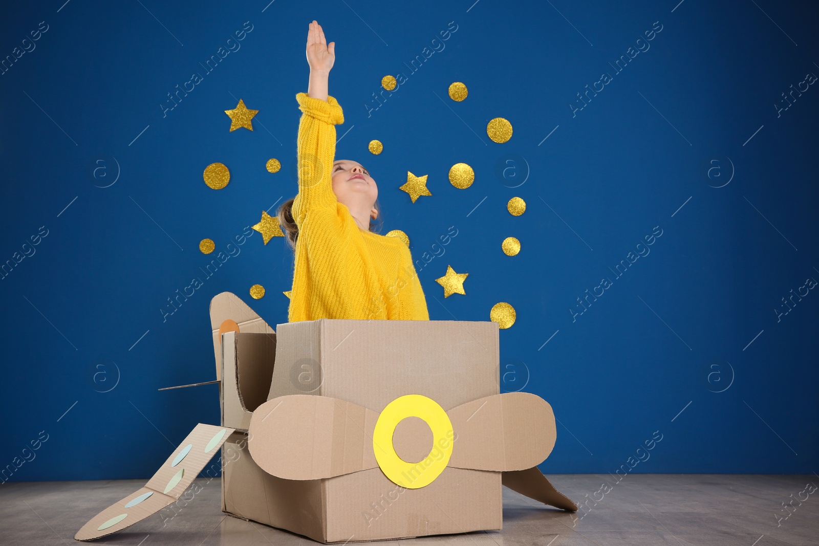 Photo of Cute little child playing with cardboard plane near blue wall