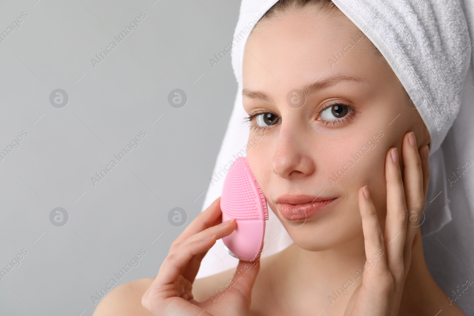 Photo of Washing face. Young woman with cleansing brush on grey background, closeup. Space for text