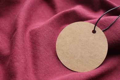 Photo of Circle shaped tag with space for text on dark red fabric, closeup