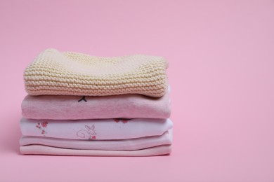 Stack of clean baby clothes on pink background. Space for text