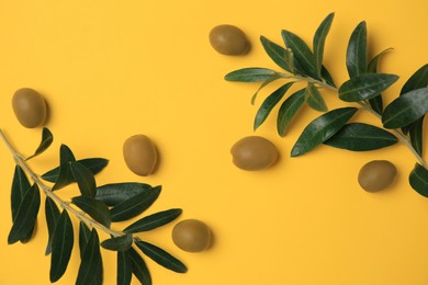 Photo of Fresh olives and green leaves on yellow background, flat lay