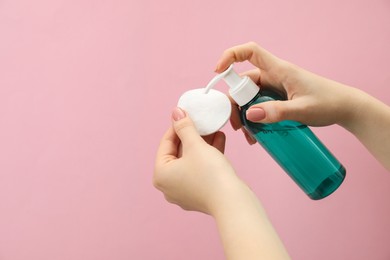 Woman applying makeup remover onto cotton pad on pink background, closeup. Space for text