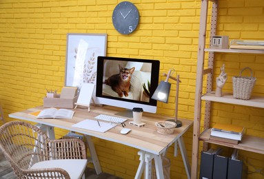 Stylish home office interior with comfortable workplace near yellow brick wall