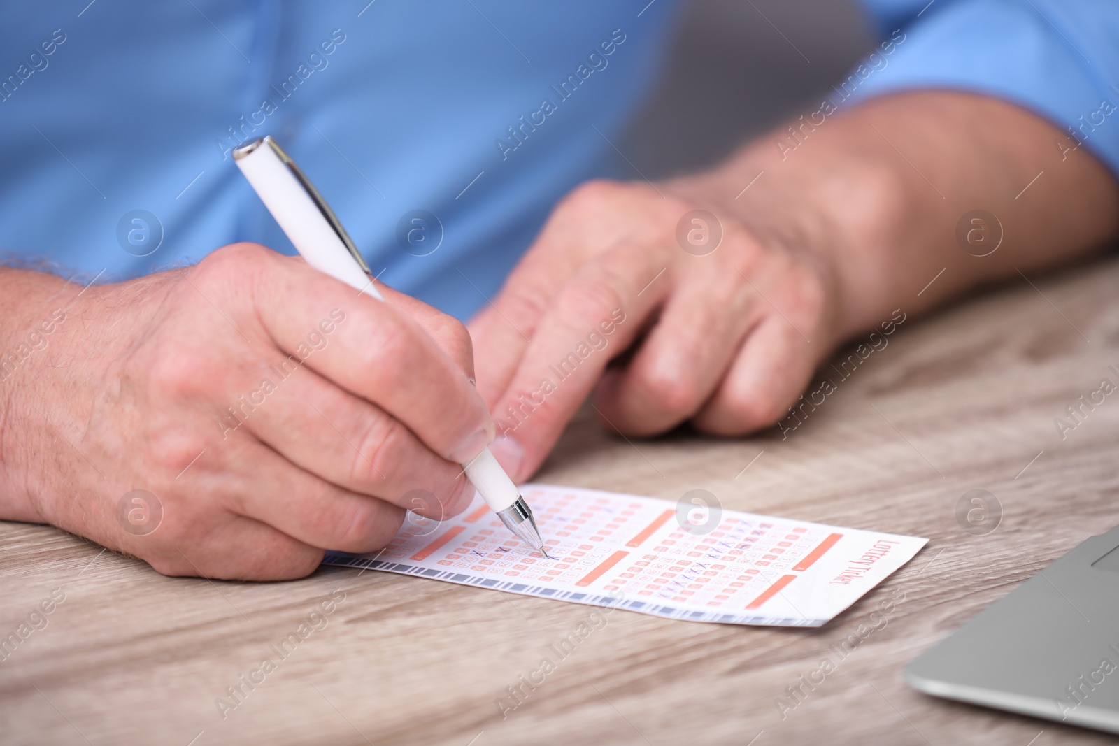 Photo of Senior man filling out lottery ticket at table, closeup
