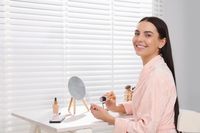 Photo of Beautiful young woman with powder and brush at dressing table indoors. Space for text